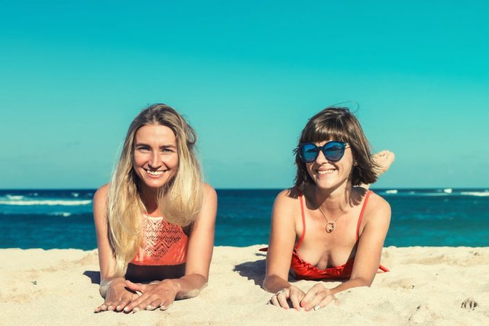 two women lying on the beach sand wearing their designer bathing suits